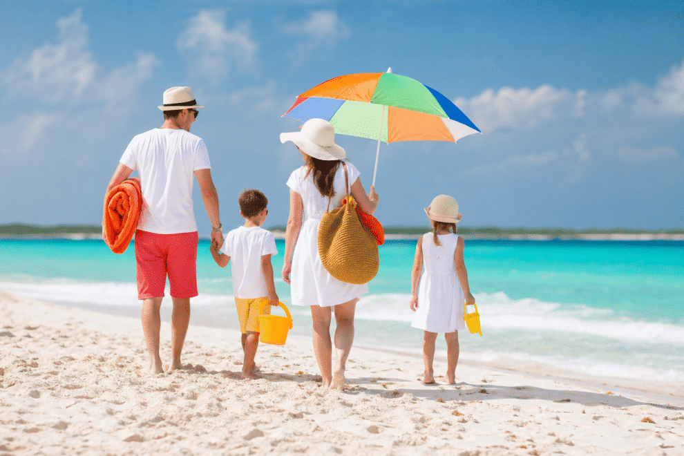 family beach trip tips - family arriving at sunny beach with gear and bags