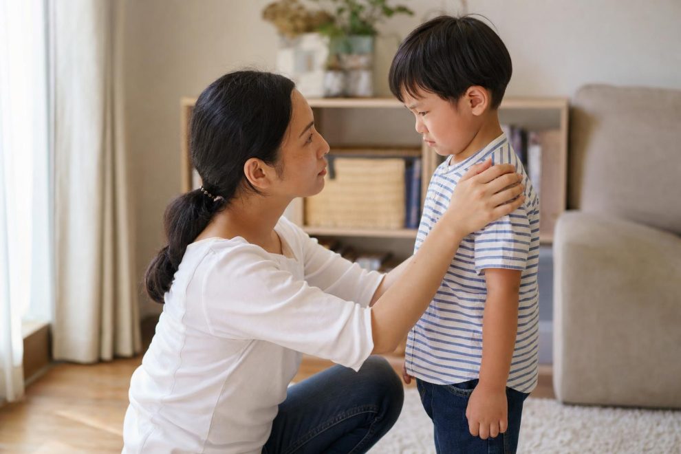 A calm parent kneeling down to gently comfort an upset young child at eye level in a bright living room, illustrating how to help kids manage big emotions