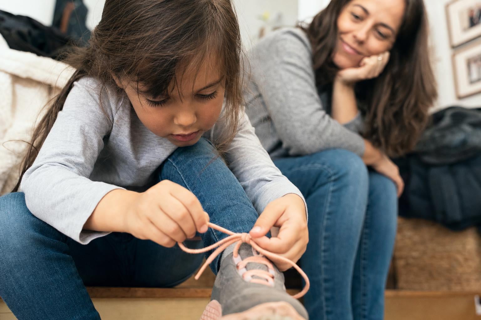 How to Build Confidence in a Child: 9 Gentle Habits That Help Them Thrive 16 A young child proudly tying their own shoelaces while a patient parent watches encouragingly nearby, warm candid documentary feel