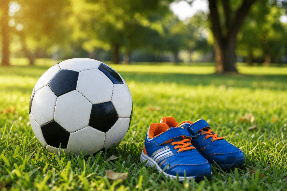 healthy competition for kids - soccer ball and children's sports shoes on green grass
