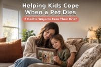 A mother sitting on the floor beside her young child who holds a dog's collar and a framed photo, looking at it together in soft window light, with a legible baked-in headline "Helping Kids Cope When a Pet Dies" and subline "7 Gentle Ways to Ease Their Grief" — a comforting scene about a family grieving a beloved pet