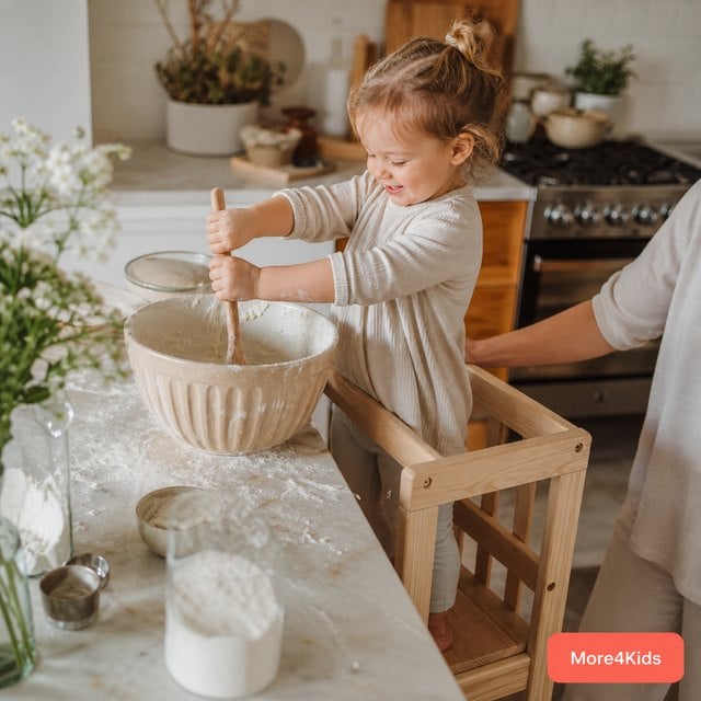 Life Skills for Tweens: Independence, Staying Home Alone, and Budgeting for Ages 10-12 20 A toddler standing in a wooden kitchen helper tower at the counter, helping stir a bowl