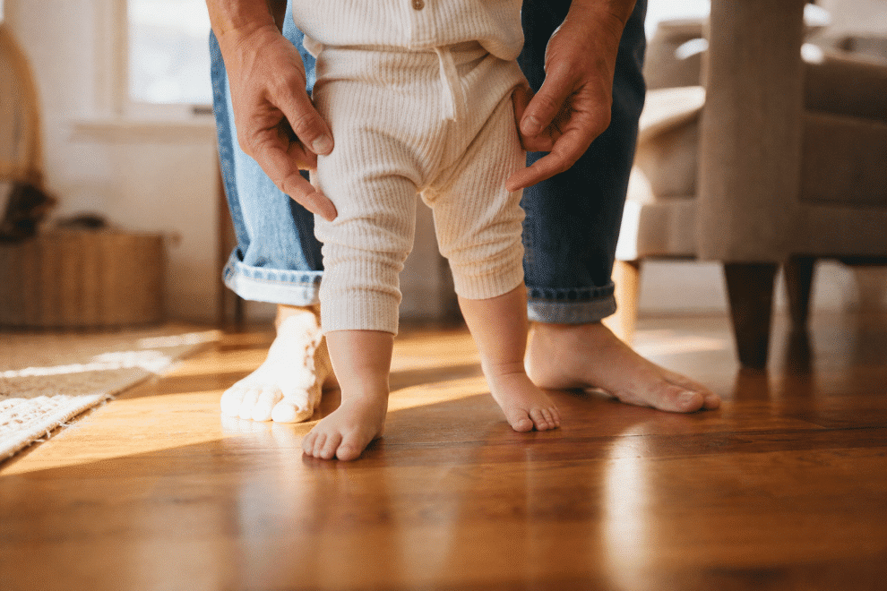 parenting toddlers - adult hands guiding toddler first steps on hardwood floor