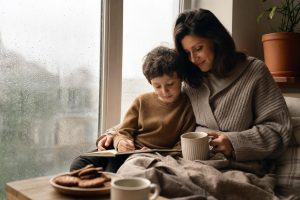 Rainy day reset — parent and children at a kitchen table with books, crayons, and a simple snack on a rainy afternoon.