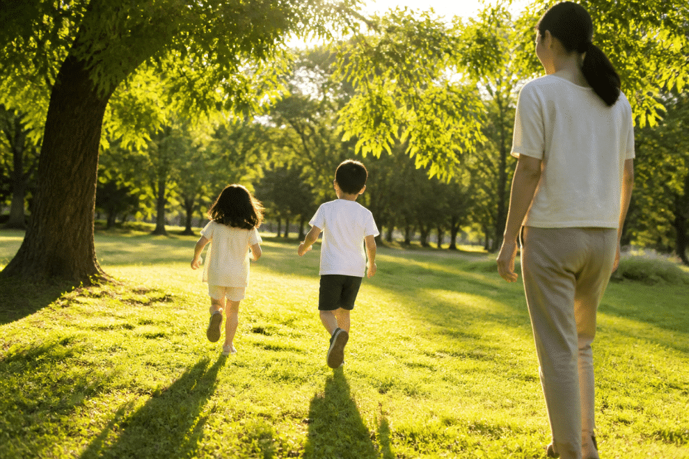 raising happy kids — family playing together in a sunny park with children running freely