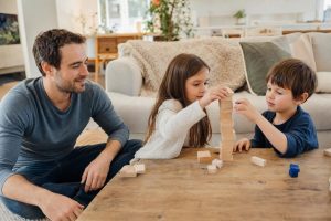 Sibling repair — parent sitting nearby while two siblings calmly work on a shared puzzle or blocks at a table, no visible conflict.