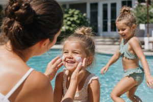Summer Safety Tips for Kids: Simple Steps for a Happy, Worry-Free Summer 15 A parent applying sunscreen to a smiling young child at a sunny backyard pool while another child plays safely nearby, illustrating practical summer safety tips for kids