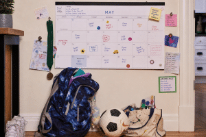 overscheduled kids - packed family calendar with backpack and sports gear piled below